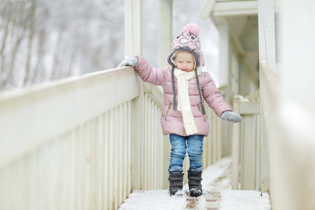 Funny little girl having fun in beautiful winter park during snowfallの写真素材