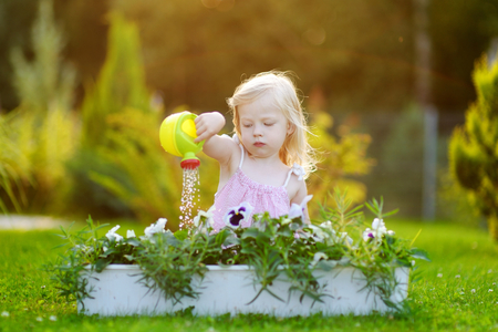 Cute little girl watering flowers in the garden at summer dayの写真素材