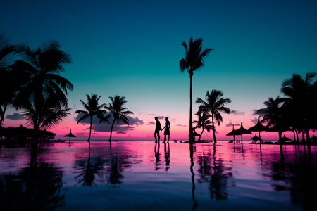 Silhouettes of young couple at scenic sunset on tropical beachの写真素材