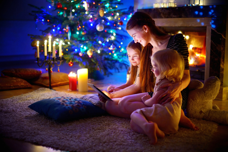 Young mother and her daughters using a tablet pc by a fireplace on warm Christmas eveningの写真素材