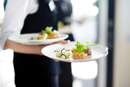 Waiter carrying plates with meat dish on some festive event, party or wedding receptionの写真素材