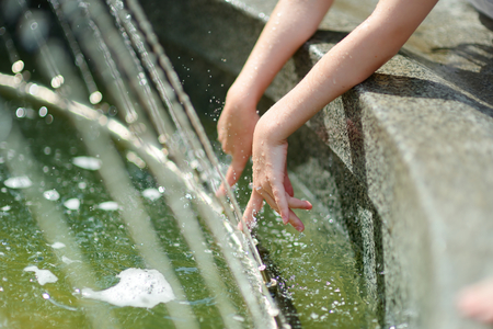 Closeup photo of child washing hands in a city fountainの写真素材