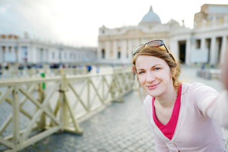 Beautiful young woman taking a picture of herself in Vatican city on summer dayの写真素材