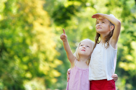 Two adorable little sisters pointing at a plane on the sky on warm and sunny summer dayの写真素材