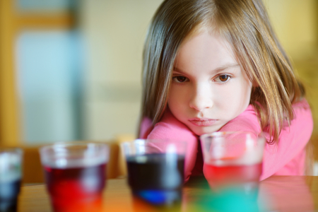 Adorable little girl painting colorful Easter eggs at homeの写真素材