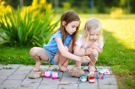 Two cute little sisters painting on stones together on hot summer dayの写真素材