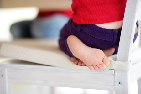 Cute little feet of a child sitting on a chair in white kitchenの写真素材