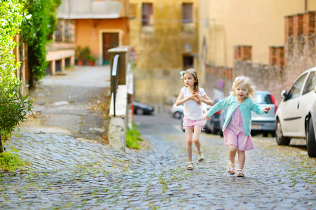 Two adorable little sisters having fun together on warm and sunny summer day in italian townの写真素材