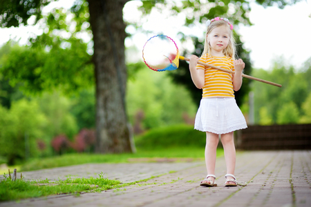 Cute little girl catching butterflies with a scoop-net on summer dayの写真素材