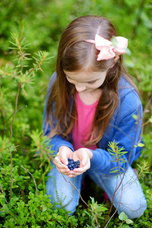 Cute little girl picking blueberries in the woods on beautiful summer dayの写真素材