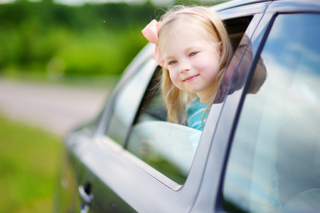 Funny little girl is sticking her head out the car window looking forward for a roadtrip or travelの写真素材