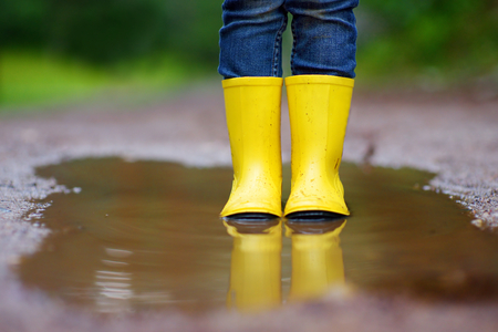 Child wearing rain boots standing in a puddle on warm summer dayの写真素材