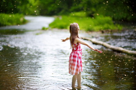 Cute little girl having fun by a river on warm and sunny summer dayの写真素材