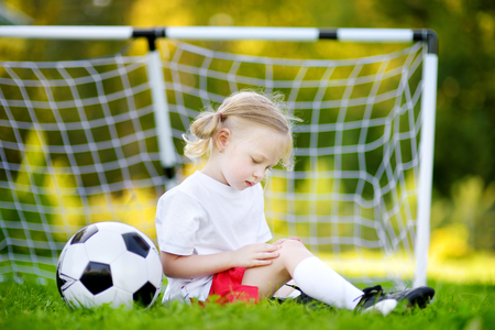 Cute little soccer player hurt her knee while defending a goal in soccer game on sunny summer dayの写真素材