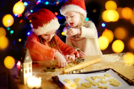 Two adorable little sisters baking Christmas cookies by a fireplace on Christmas eveの写真素材