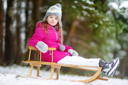 Funny little girl having fun with a sleight in beautiful winter parkの写真素材