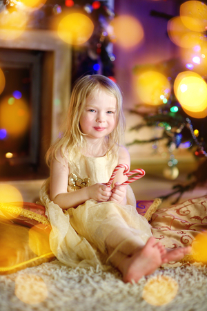 Christmas portrait of happy little girl by a fireplace in a cozy dark living room on Xmas eveの写真素材
