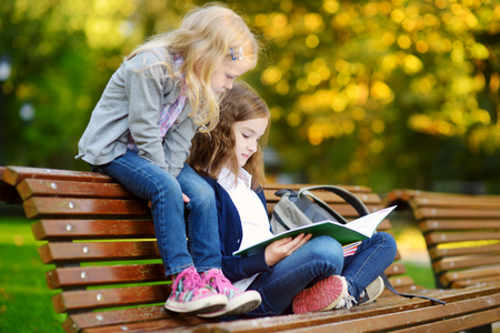 Two adorable little schoolgirls studying in a city park on bright autumn dayの写真素材