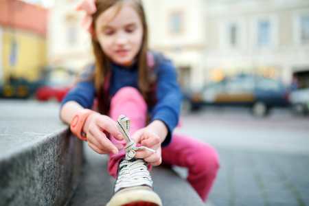 Cute little girl learning to tie shoelaces outdoors on summer dayの写真素材
