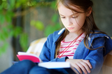 Cute little girl reading a book outdoors on warm summer dayの写真素材
