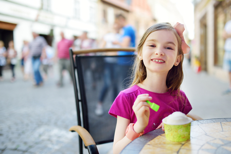Funny little girl eating ice cream in an outdoor cafe on sunny summer dayの写真素材