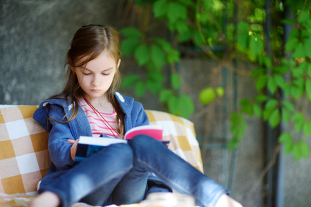 Cute little girl reading a book outdoors on warm summer dayの写真素材