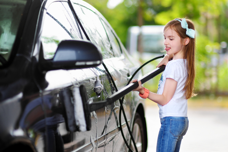 Adorable little girl washing a car on a carwash on sunny summer dayの写真素材