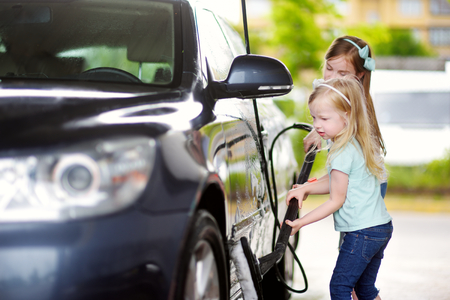 Two adorable little sisters washing a car on a carwash on sunny summer dayの写真素材