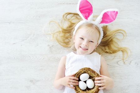 Cute little girl wearing bunny ears playing egg hunt on Easter. Adorable child celebrate Easter at home.の写真素材