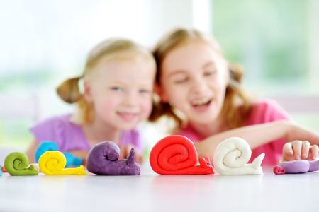 two cute little sisters having fun together with colorful modeling clay at a daycare. creative kids molding at home. children play with plasticine orの写真素材