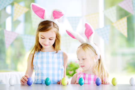 Two cute little sisters wearing bunny ears playing egg hunt on Easter. Adorable children celebrate...