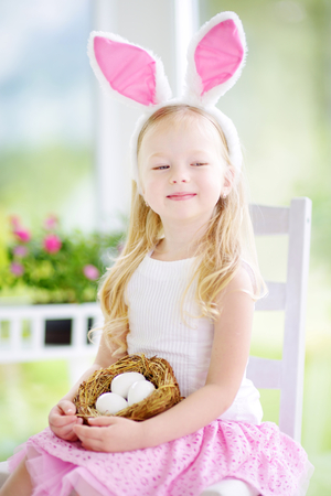 Cute little girl wearing bunny ears playing egg hunt on Easter. Adorable child celebrate Easter at home.の写真素材