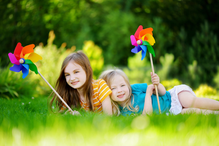 Two cute little girls holding colorful toy pinwheels on warm and sunny summer dayの写真素材