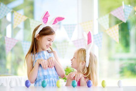 Two cute little sisters wearing bunny ears playing egg hunt on Easter. Adorable children celebrate Easter at home.の写真素材