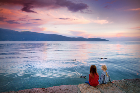 Two little girls enjoying beautiful sunset in Gargnano, a small town and comune in the province of Brescia, in Lombardy. It is situated on the western shore of Lake Garda.の写真素材