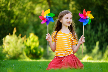 Adorable little girl holding colorful toy pinwheel on warm and sunny summer dayの写真素材