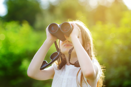 Funny little girl looking through binoculars on sunny summer dayの写真素材