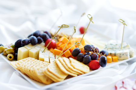 Different kinds of wine snacks: cheeses, baguettes, crackers, fruits and olives on white tableの写真素材