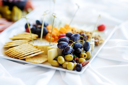 Different kinds of wine snacks: cheeses, baguettes, crackers, fruits and olives on white tableの写真素材