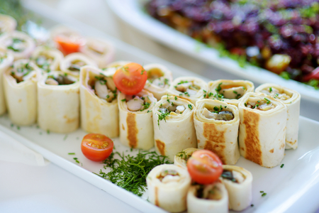 Delicious pork rolls with vegetables served on a party or wedding reception. Plates with assorted fancy finger food snacks on an event party or dinner.の写真素材