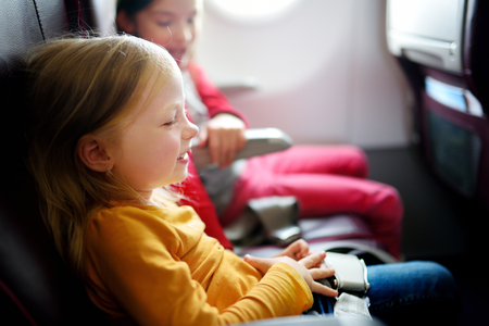 Two adorable little girls traveling by an airplane. Children sitting by aircraft window and looking outside. Traveling with kids abroad.の写真素材