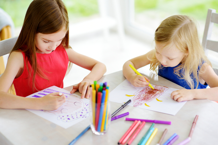 Two cute little sisters drawing with colorful pencils at a daycare. Creative kids painting together. Girls doing homework at home.の写真素材