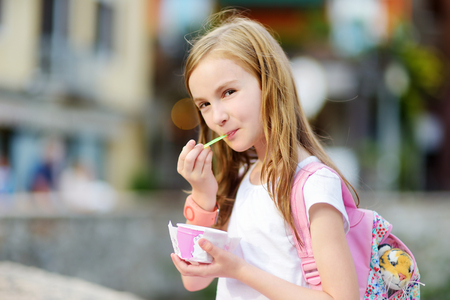 Adorable little girl eating tasty fresh ice cream outdoors on warm and sunny summer dayの写真素材