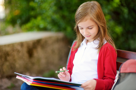 Adorable little schoolgirl studying outdoors on bright autumn day. Young student doing her homework. Education for small kids. Back to school concept.の写真素材