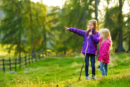 Two funny little sisters having fun during forest hike on beautiful autumn day in Italian Alps. Active leisure with small kids. Family hiking.の写真素材
