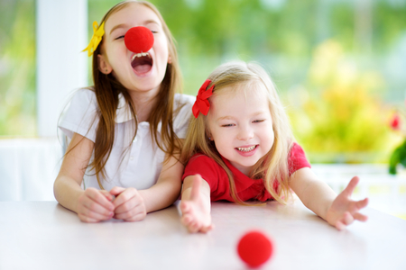 Happy little sisters wearing red clown noses having fun together on sunny summer day at home. Two kid playing together.の写真素材