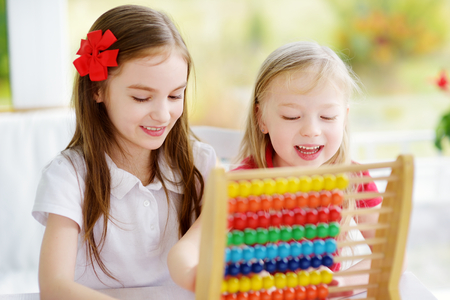 Two cute little girls playing with abacus at home. Big sister teaching her sibling to count. Smart child learning to count. Preschooler having fun with educational toy at home or kindergarten.の写真素材