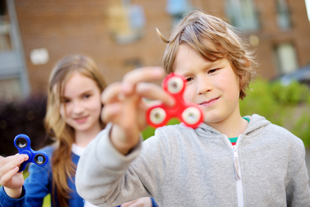 Two funny friends playing with colorful fidget spinners on the playground. Popular stress-relieving toy for school kids and adults.の写真素材