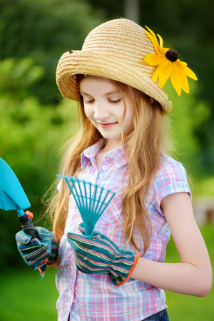 Adorable little girl wearing straw hat and childrens garden gloves holding toy garden toolsの写真素材