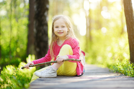 Cute little girl having fun during forest hike on beautiful summer day. Active family leisure with kids.の写真素材